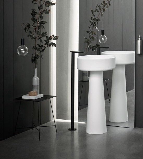 Lavabo đá nhân tạo DRL23 màu trắng mờ, kiểu dáng chân đứng loe, nổi bật trên nền tường đen hiện đại